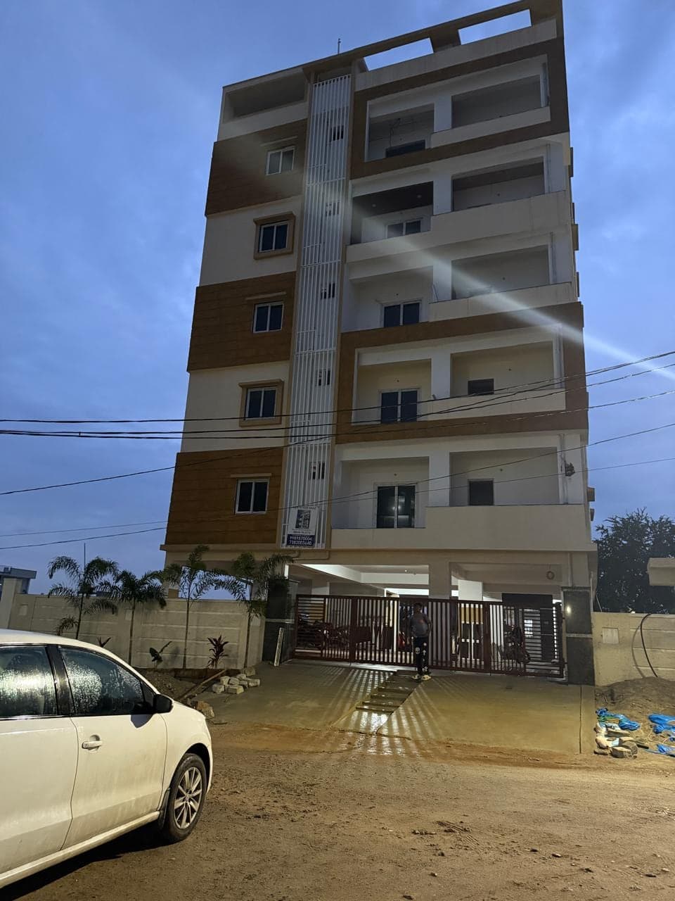 Banded-Facade Residency apartment building with tan cladding bands and a central glazed elevator shaft, photographed at dusk