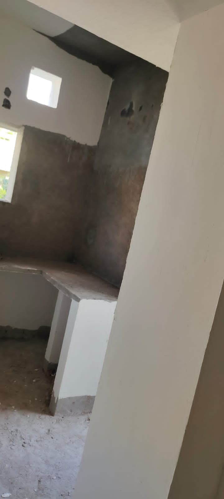 Interior corner mid-finishing, showing plastered walls and a built-in concrete counter before tiling