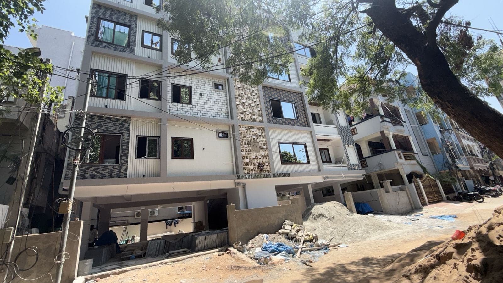 Mahalakshmi Mansion apartment building with patterned tile cladding accents, shaded by mature street trees