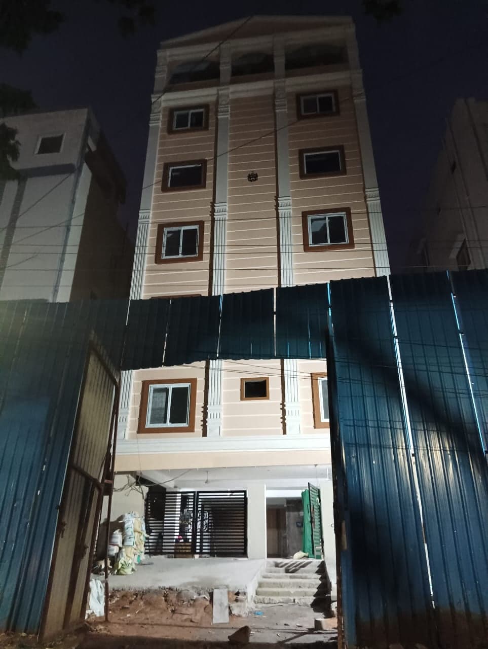Pilaster-Facade Residency apartment building lit at night, with decorative pilaster columns and a construction-site boundary fence at ground level